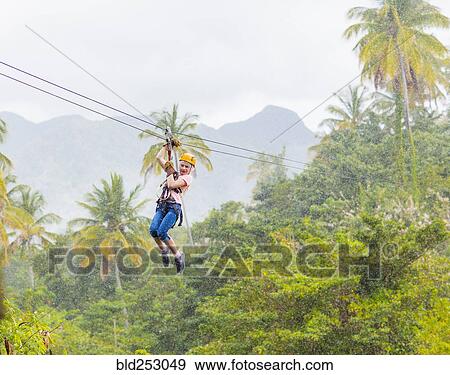 Stock Photo - Caucasian girl hanging on zip line in forest. Fotosearch
