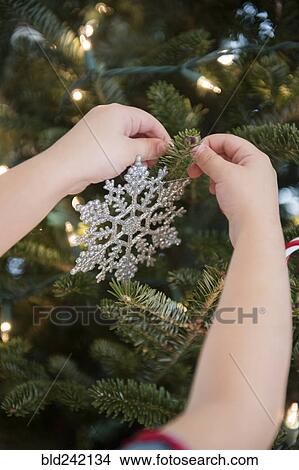 Picture - Caucasian girl hanging snowflake ornament on Christmas tree. Fotosearch
