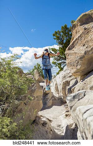 Stock Image - Caucasian girl hiking and jumping near rocks. Fotosearch