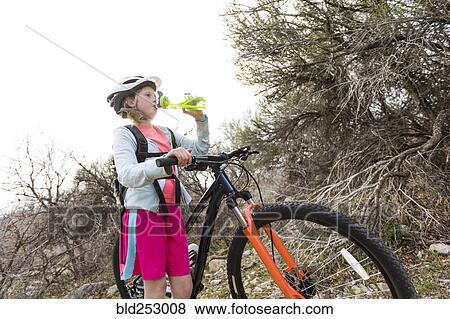Stock Photo - Caucasian girl holding bicycle and drinking water. Fotosearch