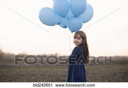 Stock Image - Caucasian girl holding blue helium balloons. Fotosearch