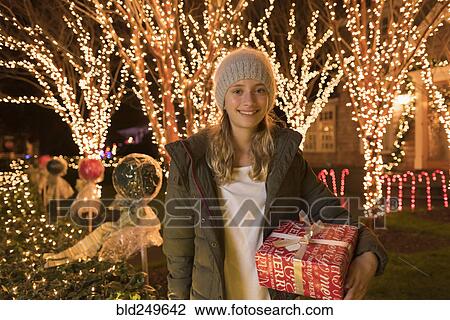 Stock Image - Caucasian girl holding Christmas gifts near house. Fotosearch
