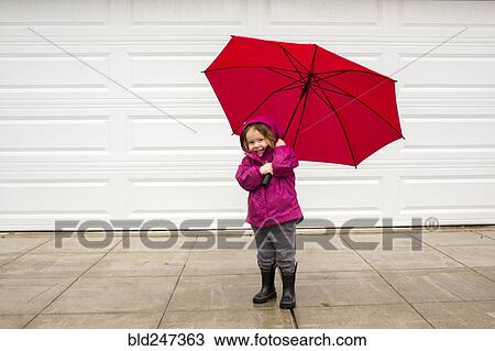 Stock Image - Caucasian girl holding red umbrella in wind. Fotosearch