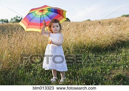 Stock Image - Caucasian girl in field with umbrella. Fotosearch