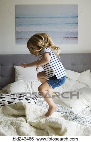 Stock Photograph - Caucasian girl jumping on bed. Fotosearch