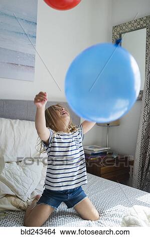 Caucasian girl kneeling on bed playing with balloons View Large Photo Image Picture - Caucasian girl kneeling on bed playing with balloons. Fotosearch