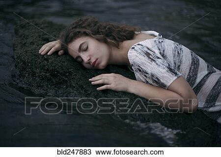 Stock Image - Caucasian girl laying face on a rock in ocean. Fotosearch