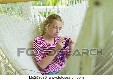 Stock Image - Caucasian girl laying in hammock and knitting. Fotosearch