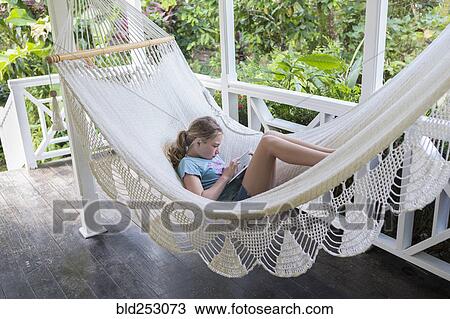 Stock Image - Caucasian girl laying in hammock using digital tablet. Fotosearch
