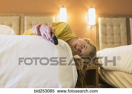 Stock Photography - Caucasian girl laying on bed in hotel room watching television. Fotosearch