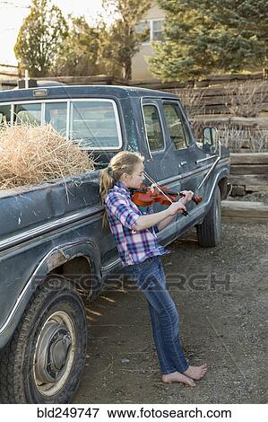 Stock Photo - Caucasian girl leaning on truck playing violin. Fotosearch