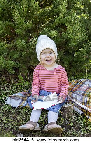 Stock Photography - Caucasian girl on blanket outdoors drawing on paper. Fotosearch