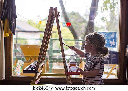 Stock Photo - Caucasian girl painting on easel near window. Fotosearch