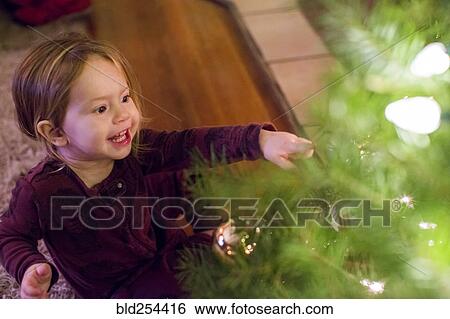 Stock Photograph - Caucasian girl pointing at ornament on Christmas tree. Fotosearch