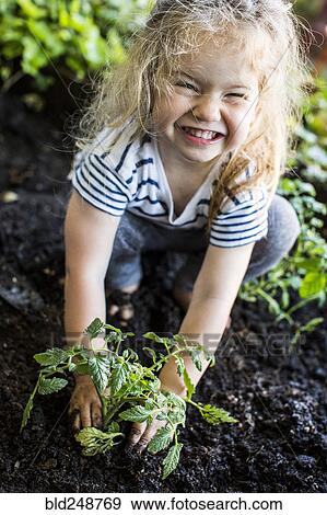 Stock Photo - Caucasian girl posing with plant in garden. Fotosearch