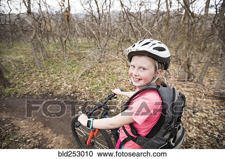 Stock Image - Caucasian girl riding bicycle on forest path. Fotosearch