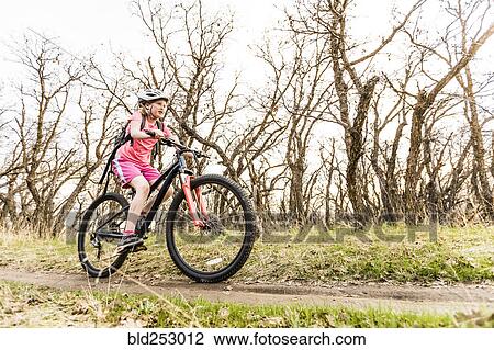Stock Image - Caucasian girl riding bicycle on forest path. Fotosearch