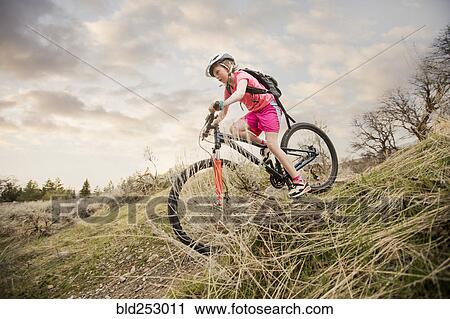 Stock Image - Caucasian girl riding bicycle on hill. Fotosearch