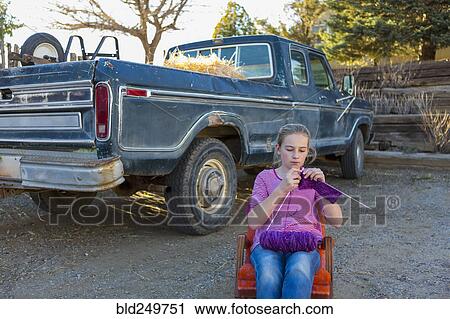 Stock Image - Caucasian girl sitting on chair near truck and knitting. Fotosearch