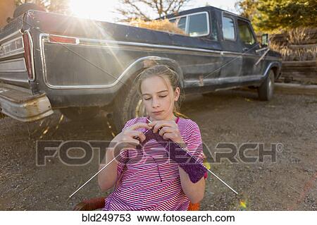 Stock Image - Caucasian girl sitting on chair near truck and knitting. Fotosearch