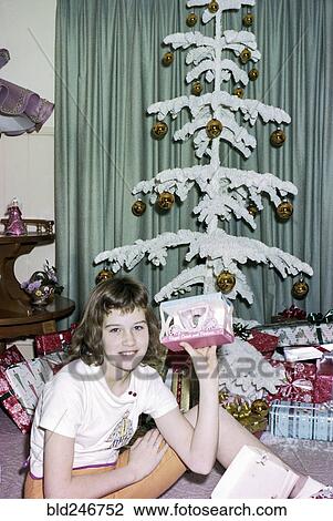 Stock Image - Caucasian girl sitting on floor showing Christmas gift. Fotosearch