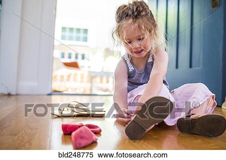 Stock Photography - Caucasian girl sitting on floor fastening sandal. Fotosearch