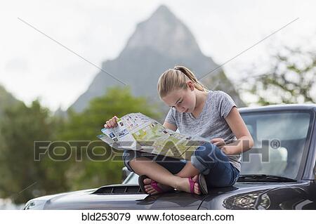 Stock Photo - Caucasian girl sitting on hood of car reading map. Fotosearch