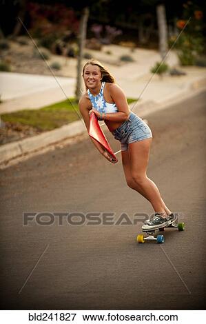 Stock Photo - Caucasian girl skateboarding on hill carrying surfboard. Fotosearch