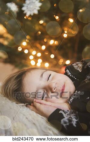 Stock Image - Caucasian girl sleeping near Christmas tree. Fotosearch