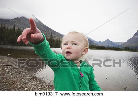 Stock Photo - Caucasian girl standing near lake pointing. Fotosearch