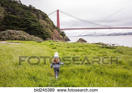 Stock Photo - Caucasian girl walking in grass near bridge. Fotosearch