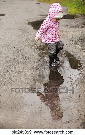 Stock Photo - Caucasian girl wearing boots splashing in puddle. Fotosearch