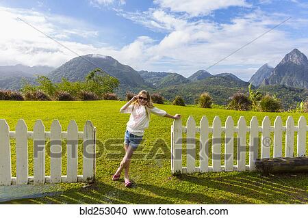 Stock Image - Caucasian girl wearing sunglasses leaning on fence. Fotosearch