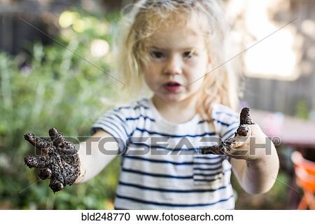 Stock Image - Caucasian girl with muddy hands in garden. Fotosearch