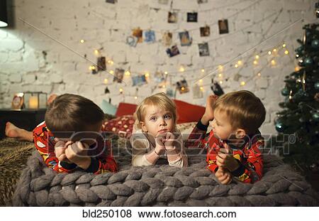 Caucasian girls and boy laying on bed near Christmas tree View Large Photo Image Stock Photo - Caucasian girls and boy laying on bed near Christmas tree. Fotosearch