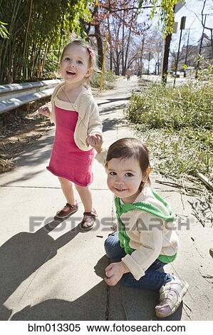 Stock Photography - Caucasian girls holding hands on sidewalk. Fotosearch