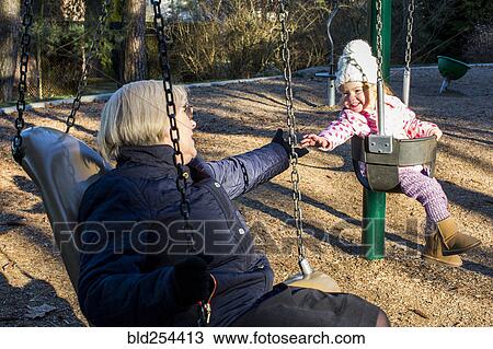 Stock Image - Caucasian grandmother and granddaughter on swings. Fotosearch