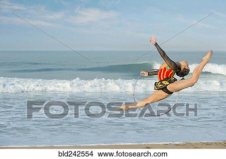 Picture - Caucasian gymnast jumping with hoop on beach. Fotosearch
