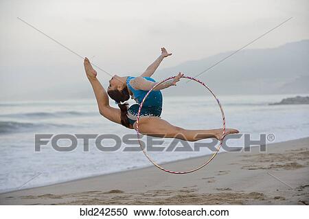 Stock Image - Caucasian gymnast jumping with hoop on beach. Fotosearch