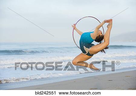 Stock Image - Caucasian gymnast jumping with hoop on beach. Fotosearch