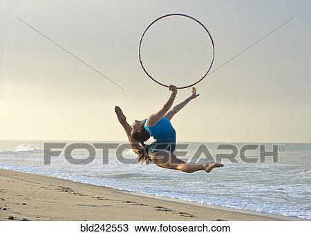 Stock Image - Caucasian gymnast jumping with hoop on beach. Fotosearch