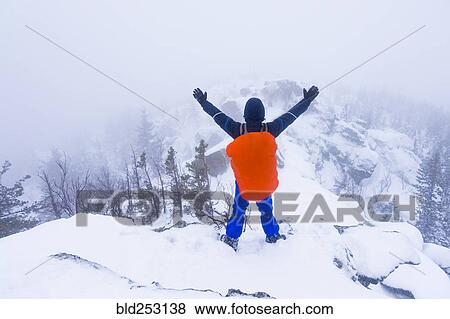 Stock Photo - Caucasian hiker waving on snow covered mountain. Fotosearch