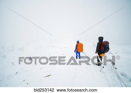 Stock Image - Caucasian hikers carrying skis on mountain. Fotosearch