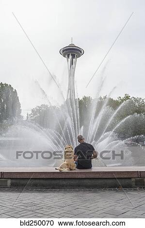Stock Image - Caucasian man and dog sitting on fountain near tower. Fotosearch