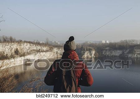 Stock Image - Caucasian man at the edge of reservoir wearing backpack. Fotosearch