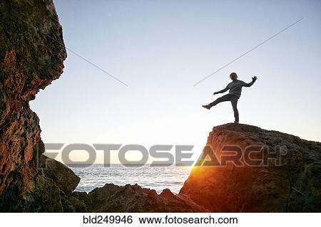 Stock Photograph - Caucasian man balancing on rock at ocean. Fotosearch