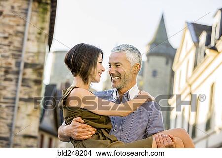 Picture - Caucasian man carrying a woman in city. Fotosearch