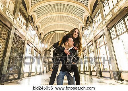 Stock Photograph - Caucasian man carrying woman piggyback in lobby. Fotosearch