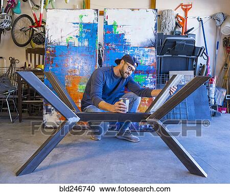 Stock Image - Caucasian man crouching and examining metal sculpture. Fotosearch