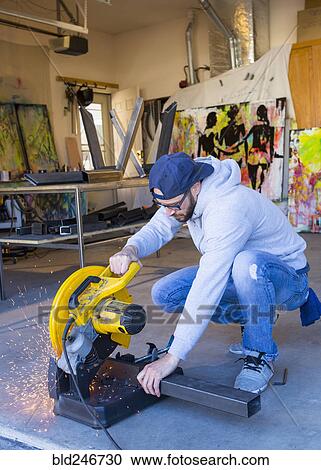 Stock Image - Caucasian man cutting metal with saw. Fotosearch